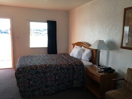 Una habitación de hotel con una cama, un escritorio con lámpara, una silla y una ventana con cortinas.