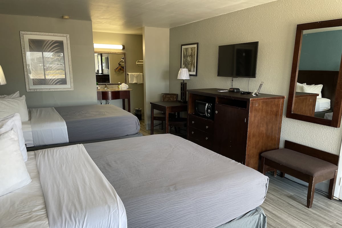 A hotel room with two beds, a desk, a TV, a mirror, and a microwave.