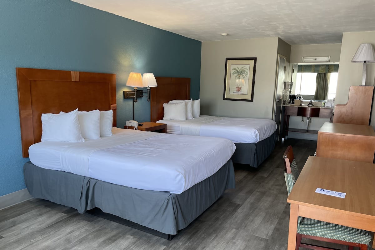 A hotel room with two beds, a desk, a chair, a lamp, a phone, and a framed picture on the wall.