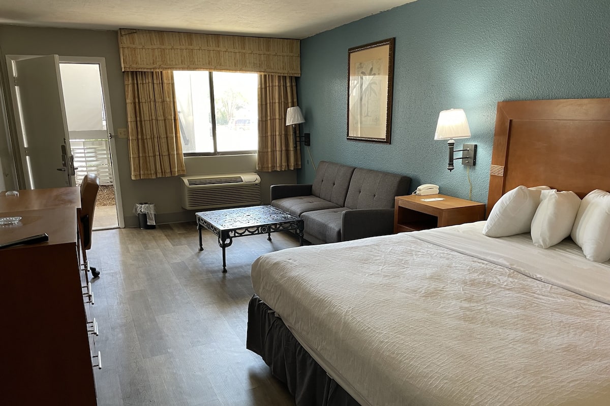 A hotel room with a bed, a desk, a sofa, a table, and a window with curtains.
