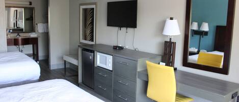 A hotel room with two beds, a desk with a chair, a flat-screen TV, a microwave, and a large mirror.