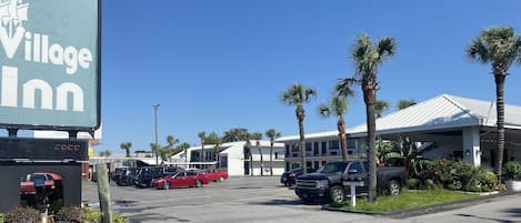 A parking lot with several cars, a large sign for Village Inn, and a building with a white roof and palm trees.