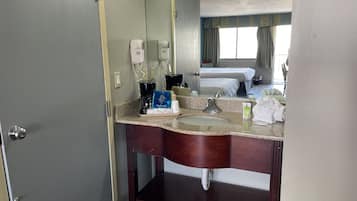 Ein Hotelbadezimmer mit Marmorwaschbecken, einem Spiegel, einem Föhn, einer Kaffeemaschine und einem Handtuchhalter.