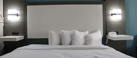 Una habitación de hotel con una cama grande, dos mesitas de noche con lámparas y un cabecero sencillo.