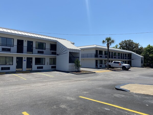 Un motel de varios pisos, cada uno con balcones y un estacionamiento al frente.