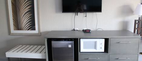 A compact kitchenette with a microwave, refrigerator, and a flat-screen TV mounted on the wall.