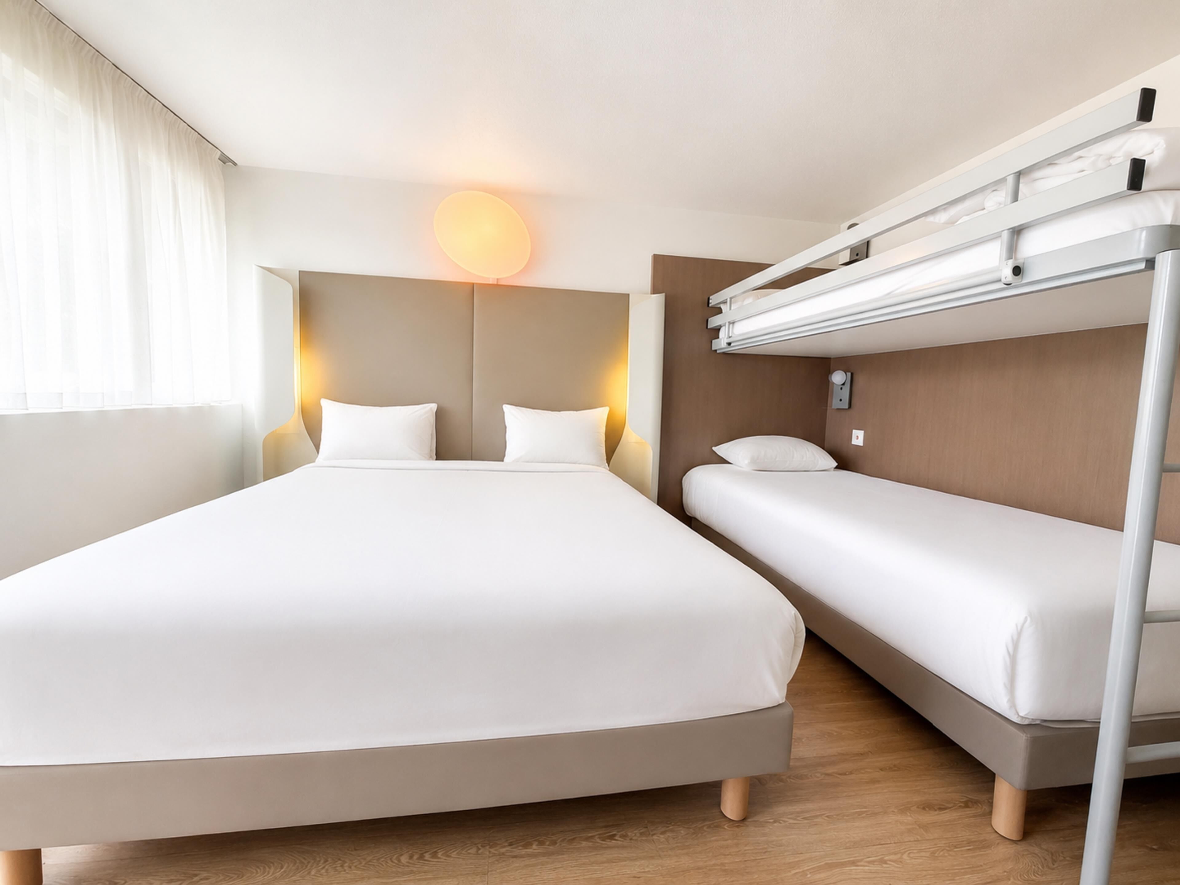 Een hotelkamer met een groot bed, een kleiner bed en een stapelbed.