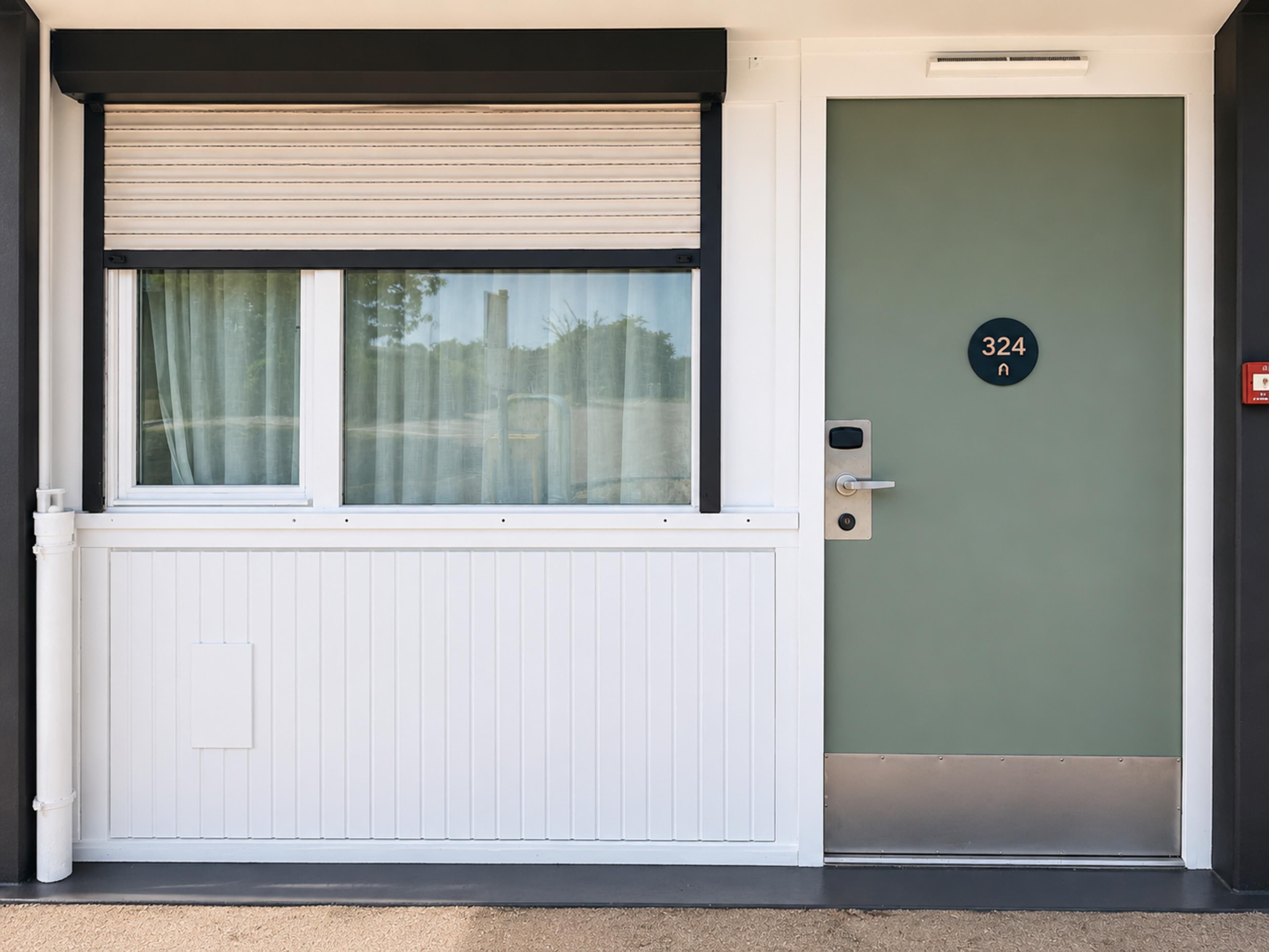 Une porte avec une plaque numérotée, une fenêtre avec un store enrouleur et un chambranle de porte blanc.
