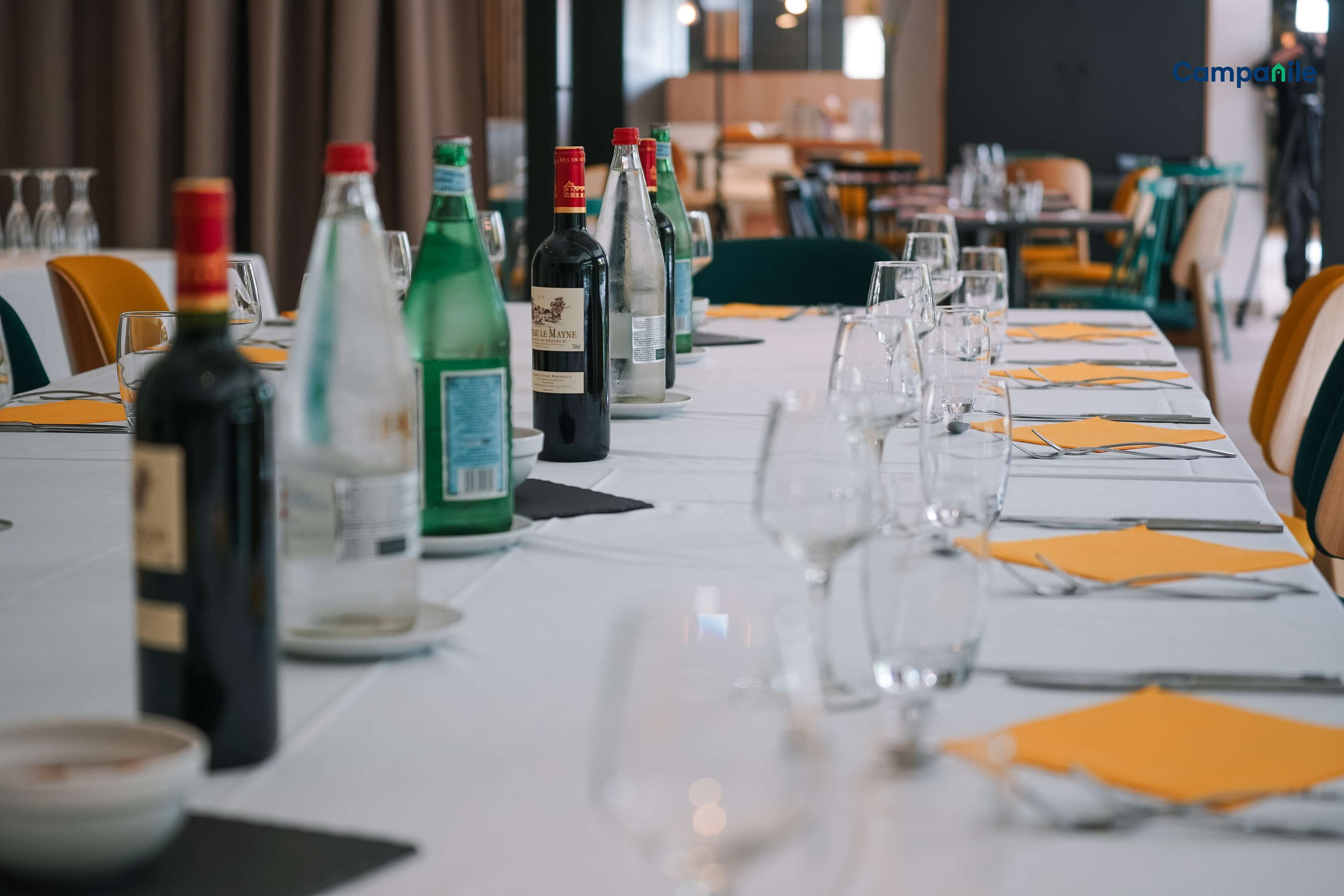 Une table dressée dans un restaurant, avec des bouteilles de vin, des verres et des serviettes orange.