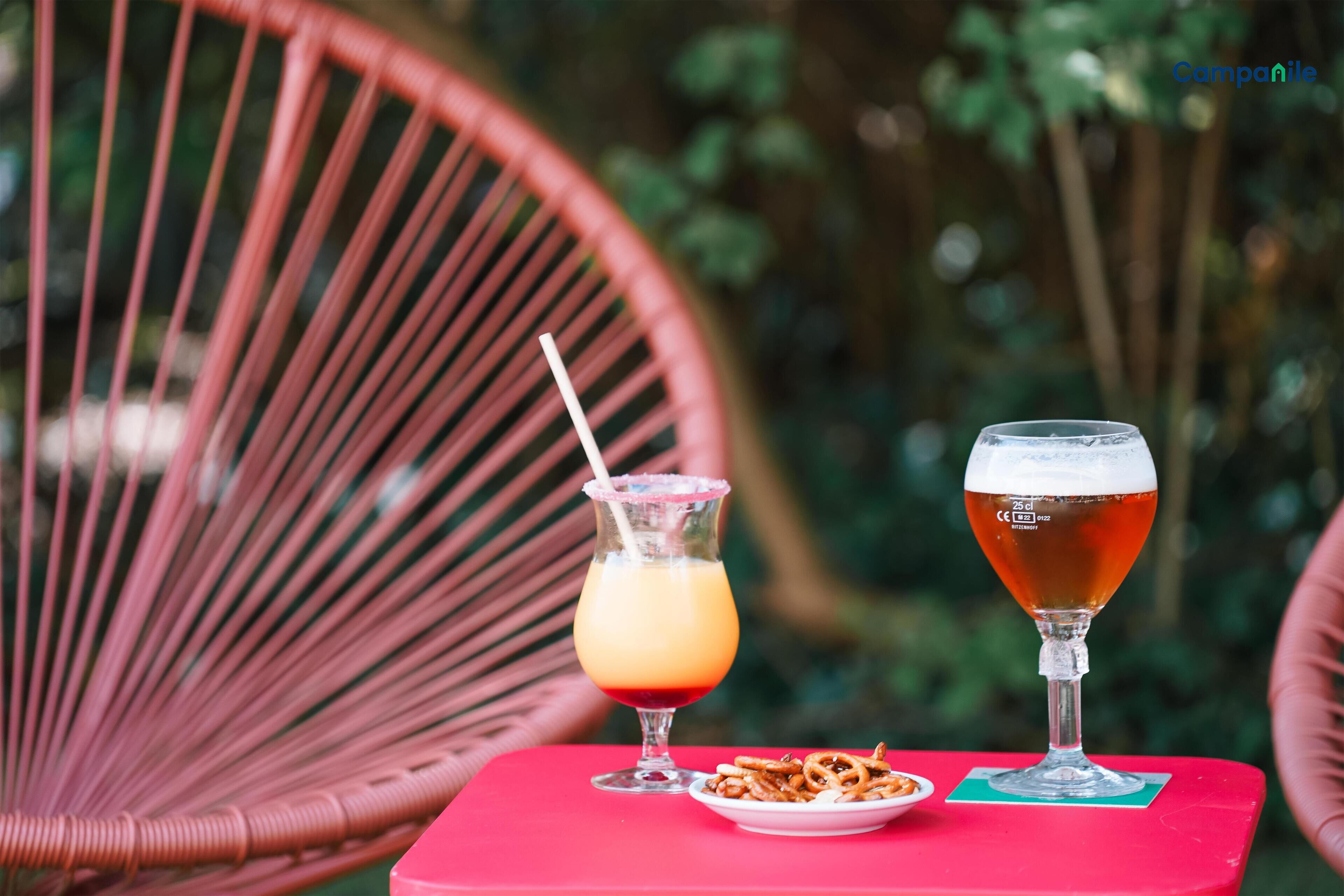 Two drinks on a red table with a plate of pretzels.