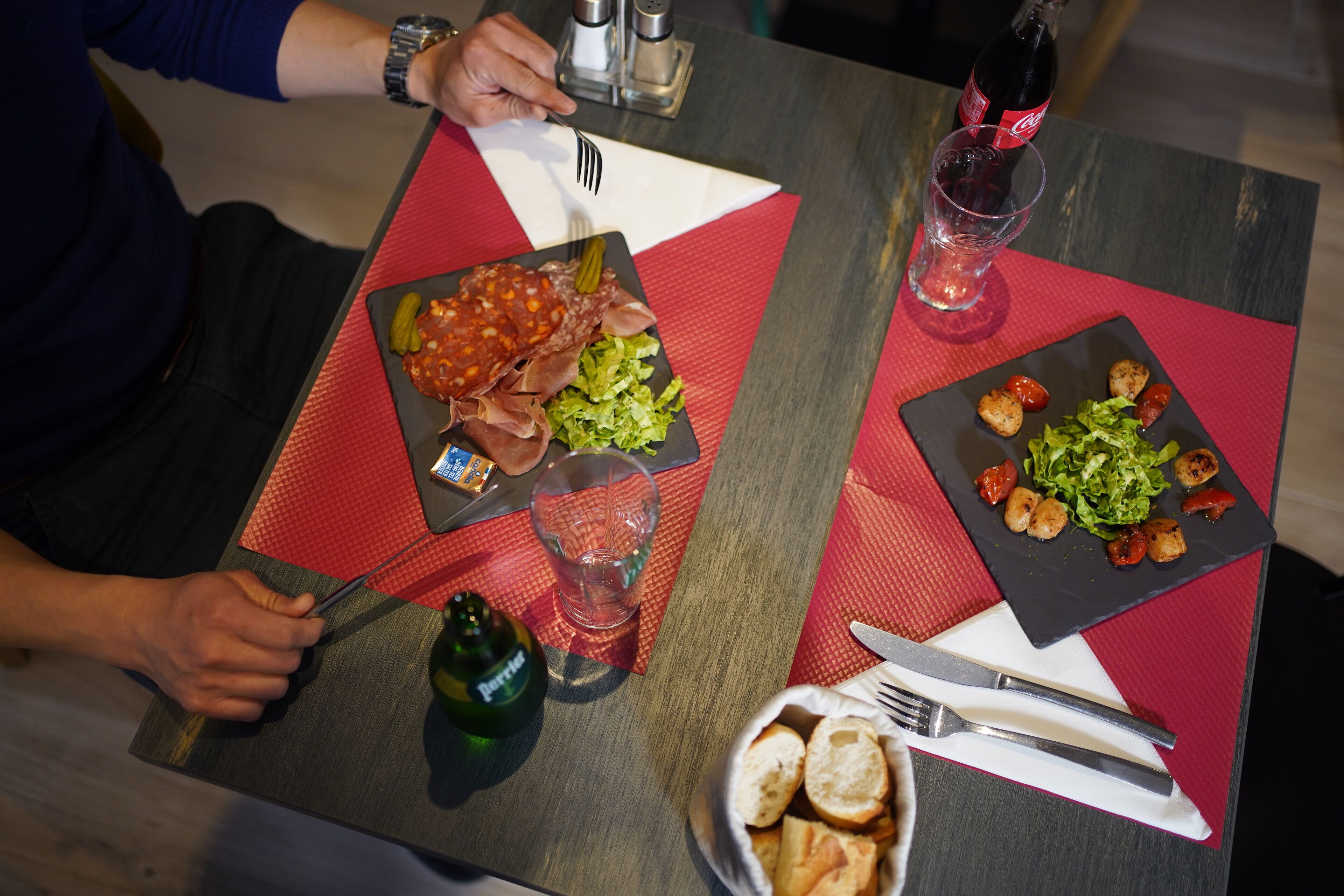 Una mesa de comedor con dos platos de comida, cubiertos, una botella y vasos.