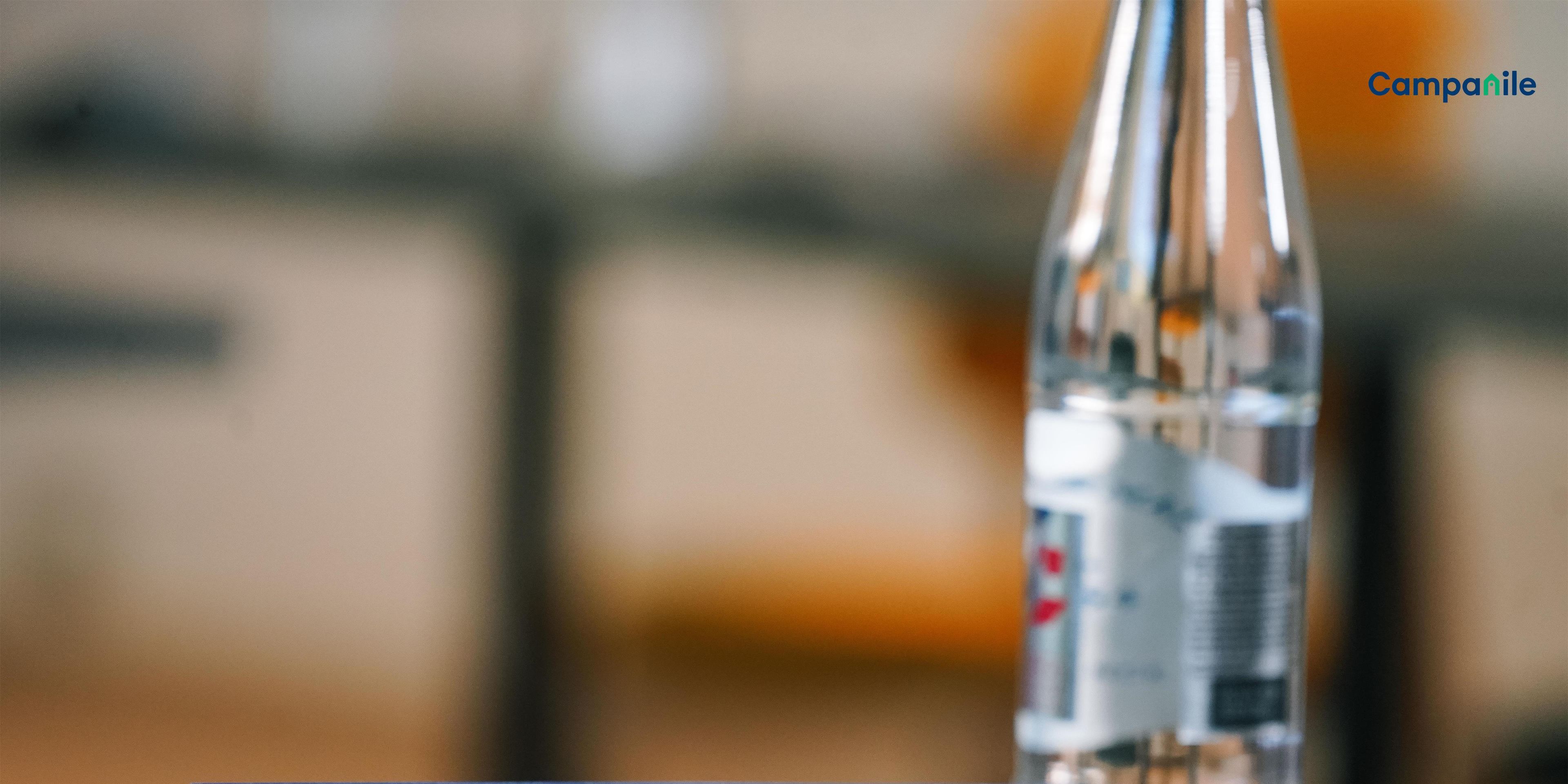 A welcome sign with "BIENVENUE WELCOME" and "Campanile" branding, a clear bottle, and a blurred background.