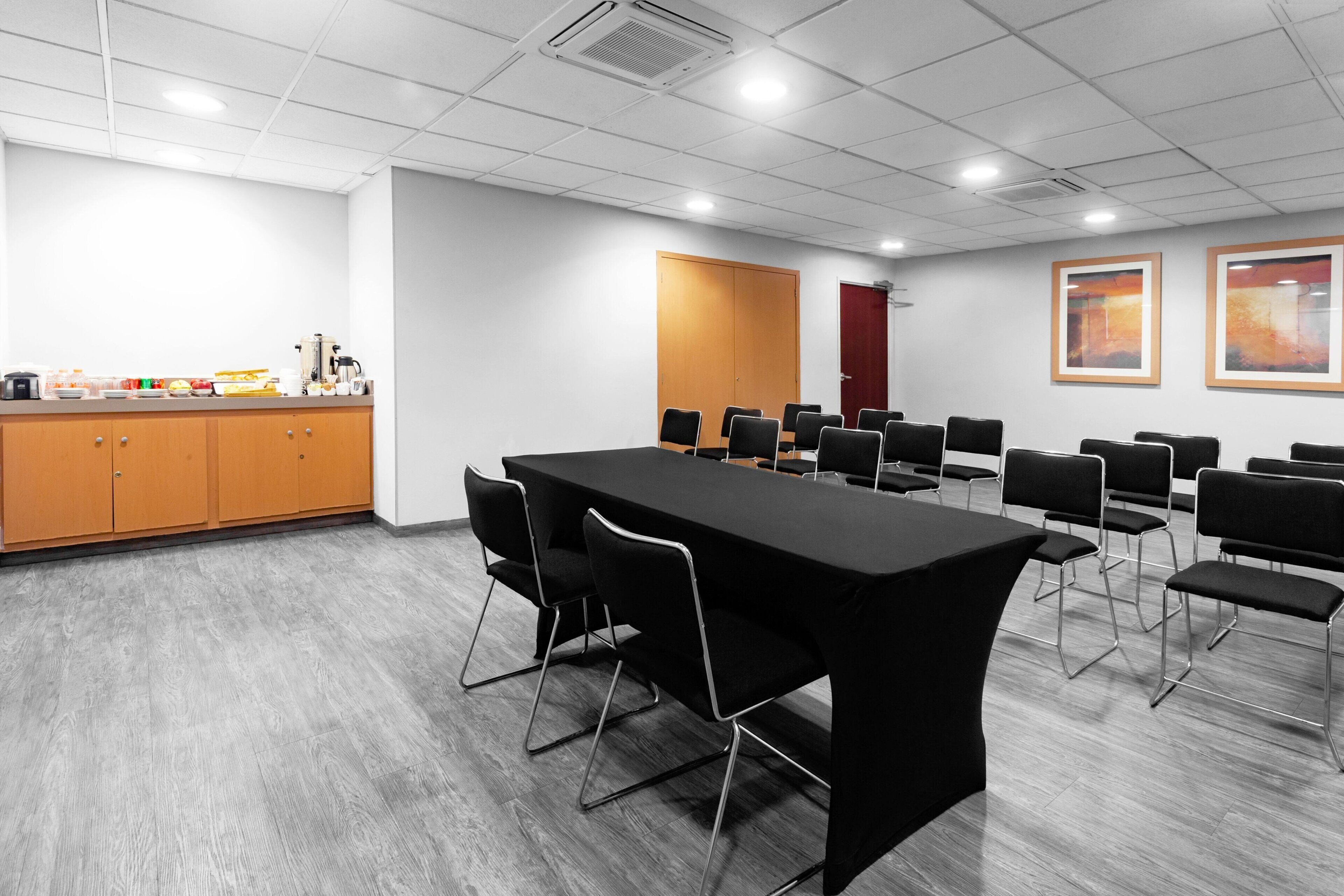 Un salón de conferencias con una larga mesa, sillas negras, un armario de madera y una puerta.