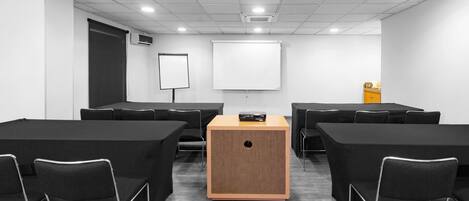 Un salón de conferencias con un atril central, sillas negras, una pizarra y una pantalla para proyector.