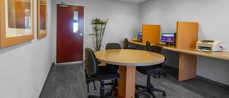 A conference room with a round table, four chairs, a computer, and a printer.