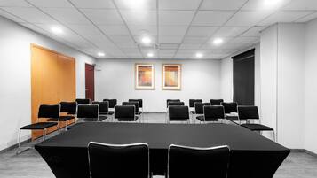 Un salón de conferencias con una larga mesa, varias sillas, dos obras de arte enmarcadas en la pared y una pantalla para proyector.