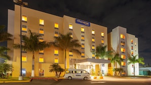A CityExpress hotel at night with illuminated windows, palm trees, and a white van parked in front. - City Express by Marriott Celaya Parque (Celaya)