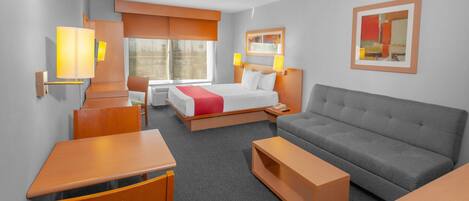 A hotel room with a bed, a grey sofa, a wooden table, and a small wooden cabinet.