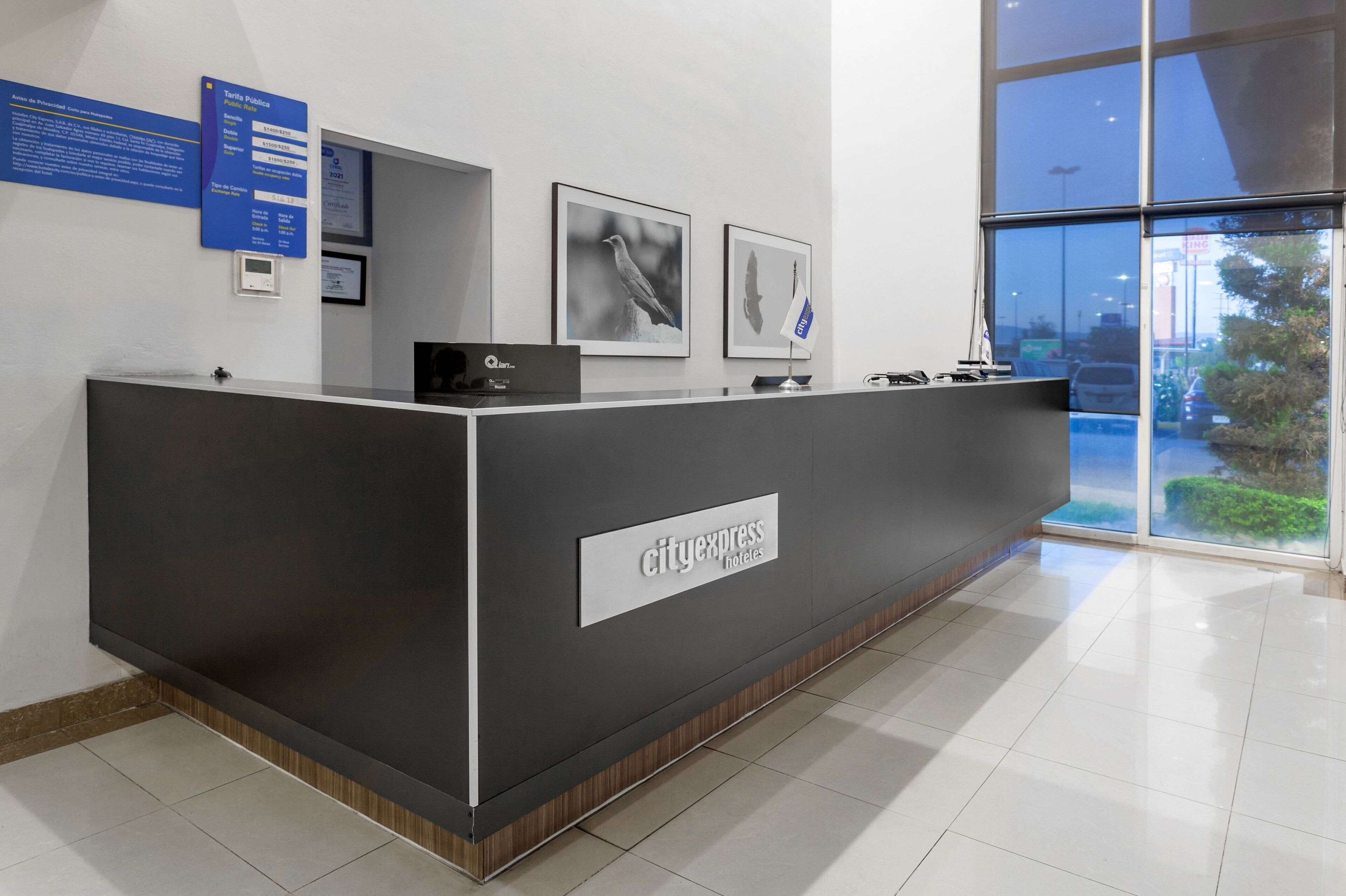 A reception desk with a CityExpress Hotels sign, framed bird photographs, and a blue informational board.