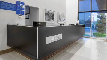 A reception desk with a CityExpress Hotels sign, framed bird photographs, and a blue informational board.