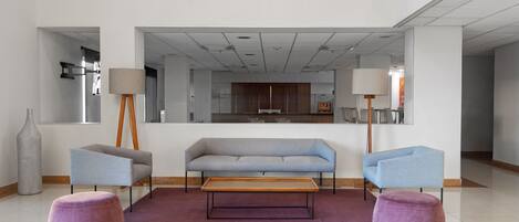 Un vestíbulo moderno con un sofá gris, dos sillones, una mesa de centro de madera y otomanas moradas.