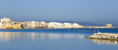 A coastal cityscape with buildings along the waterfront, calm sea, and rocky breakwaters.