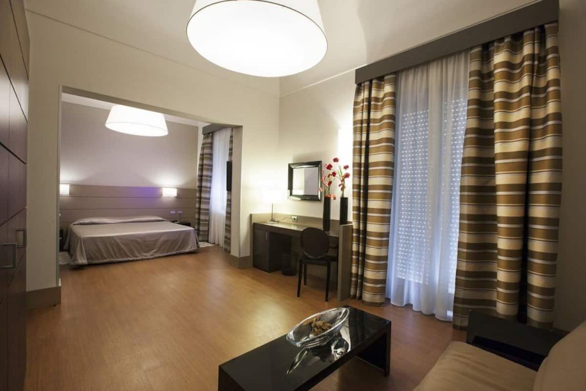 A hotel room with a bed, a desk, a chair, a coffee table, and curtains.