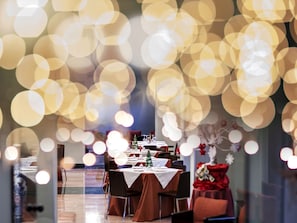 Uma sala de jantar com mesas postas para uma refeição, cadeiras e um enfeite de árvore de Natal.