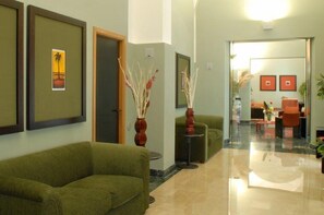 Um hall com sofás verdes, obras de arte emolduradas e uma mesa de centro de vidro.