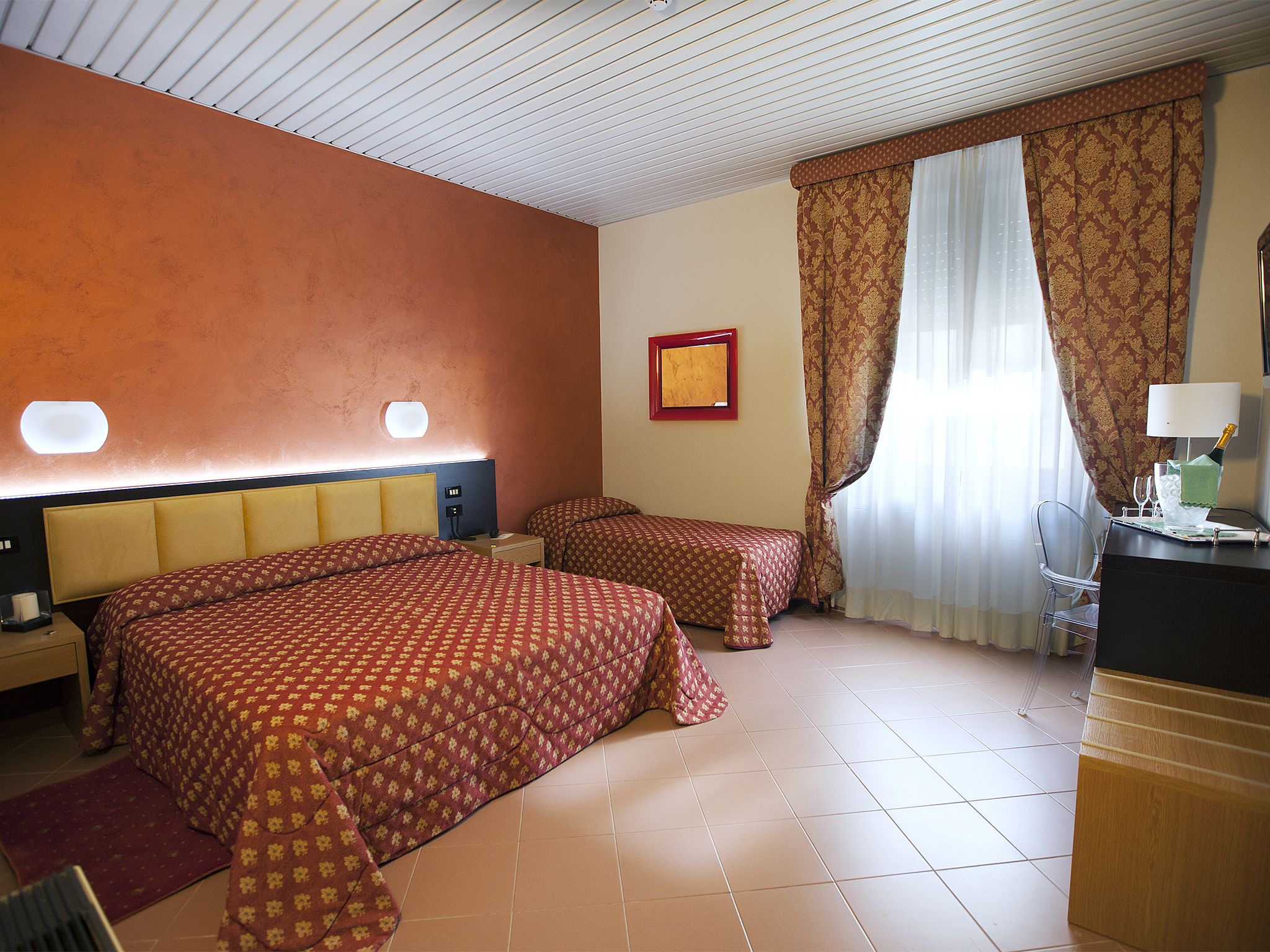 Een hotelkamer met twee bedden, een bureau, een stoel, een lamp en een fles champagne.