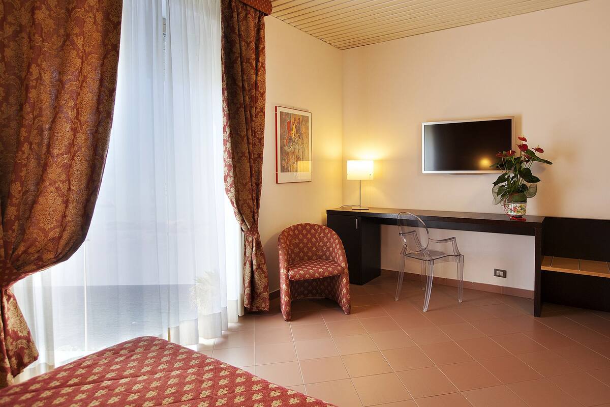 A hotel room with a bed, a desk, a chair, a TV, and a window with curtains.