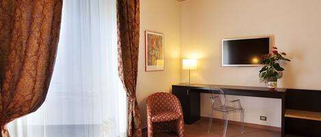 A hotel room with a bed, a desk, a chair, a TV, and a window with curtains.