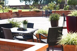 An outdoor patio area with brick walls, potted plants, and metal chairs and tables.