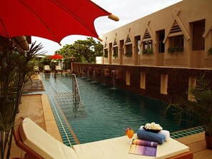 An indoor swimming pool with a red umbrella, lounge chairs, and a table with towels and a drink. - Maninarakorn Hotel (Chiang Mai)