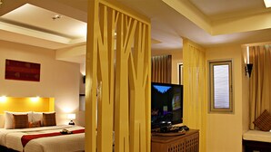 Une chambre d’hôtel équipée d’un lit, d’une télévision, d’un coin salon et d’une fenêtre avec des stores.