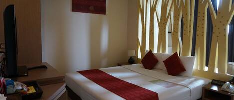 Habitación de hotel con cama, escritorio con computadora, televisor y ventana con cortinas.