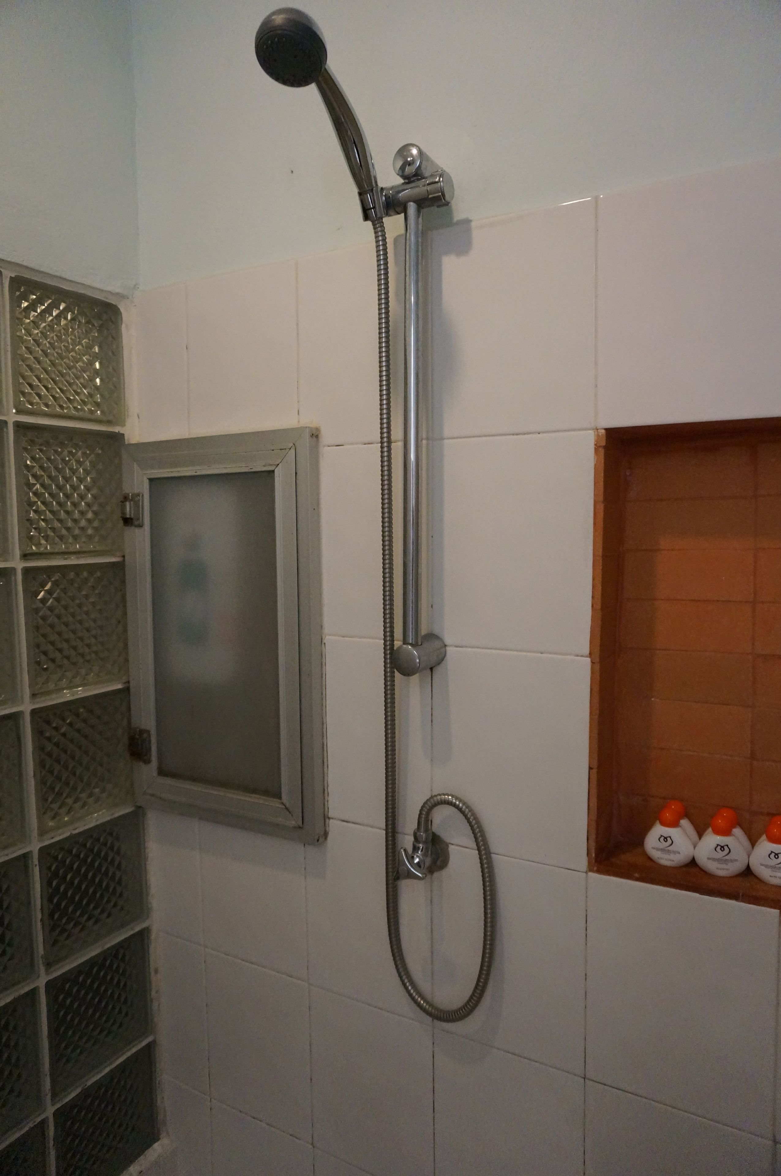 Eine Dusche mit Handbrause und Deckenbrause, eine Milchglasschiebetür und ein Ablagebereich mit Flaschen.