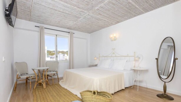 A bedroom with a bed, a bedside table, a chair, a mirror, and a window. - Can Beia Hostal Boutique (Sant Antoni de Portmany)