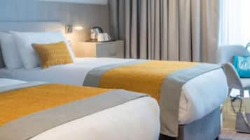 A hotel room with two beds, a nightstand, a lamp, and a view of the outdoors.