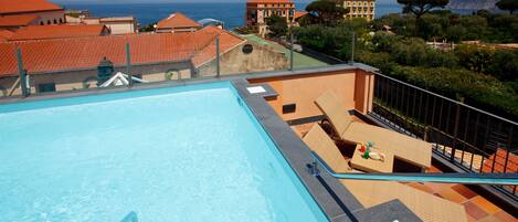 Una piscina en la azotea con vistas despejadas al mar y edificios al fondo.