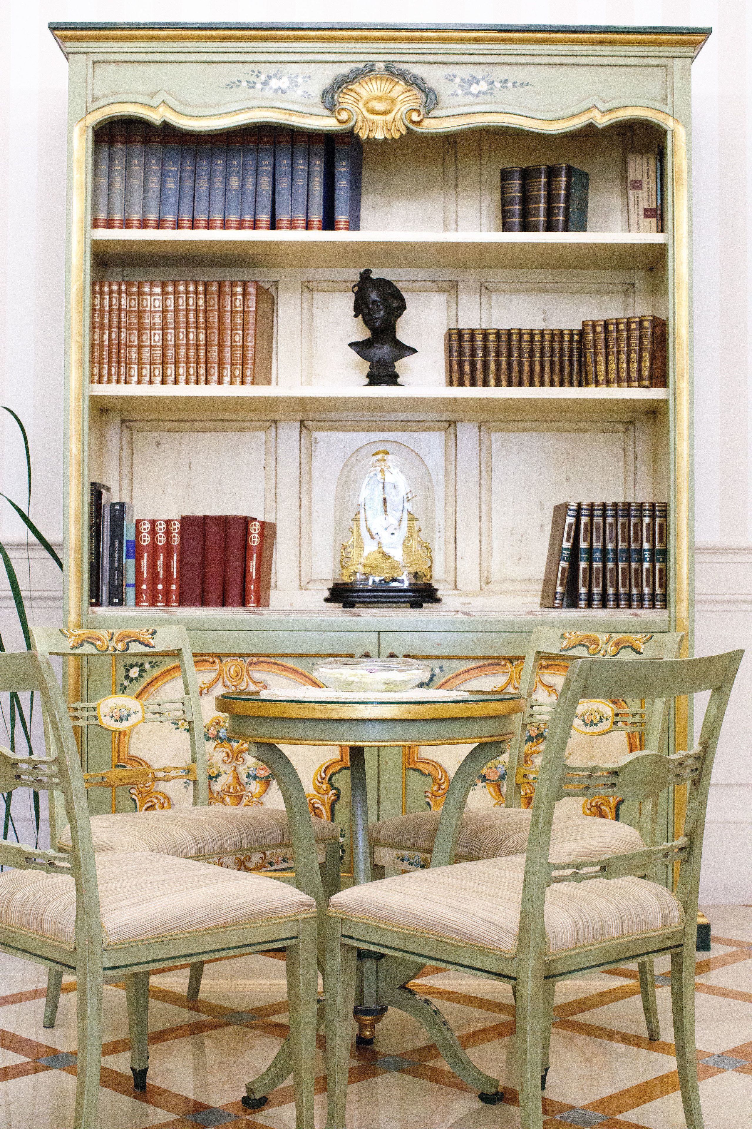 Una estantería de estilo antiguo con varias repisas, una mesa decorativa y sillas ornamentadas.