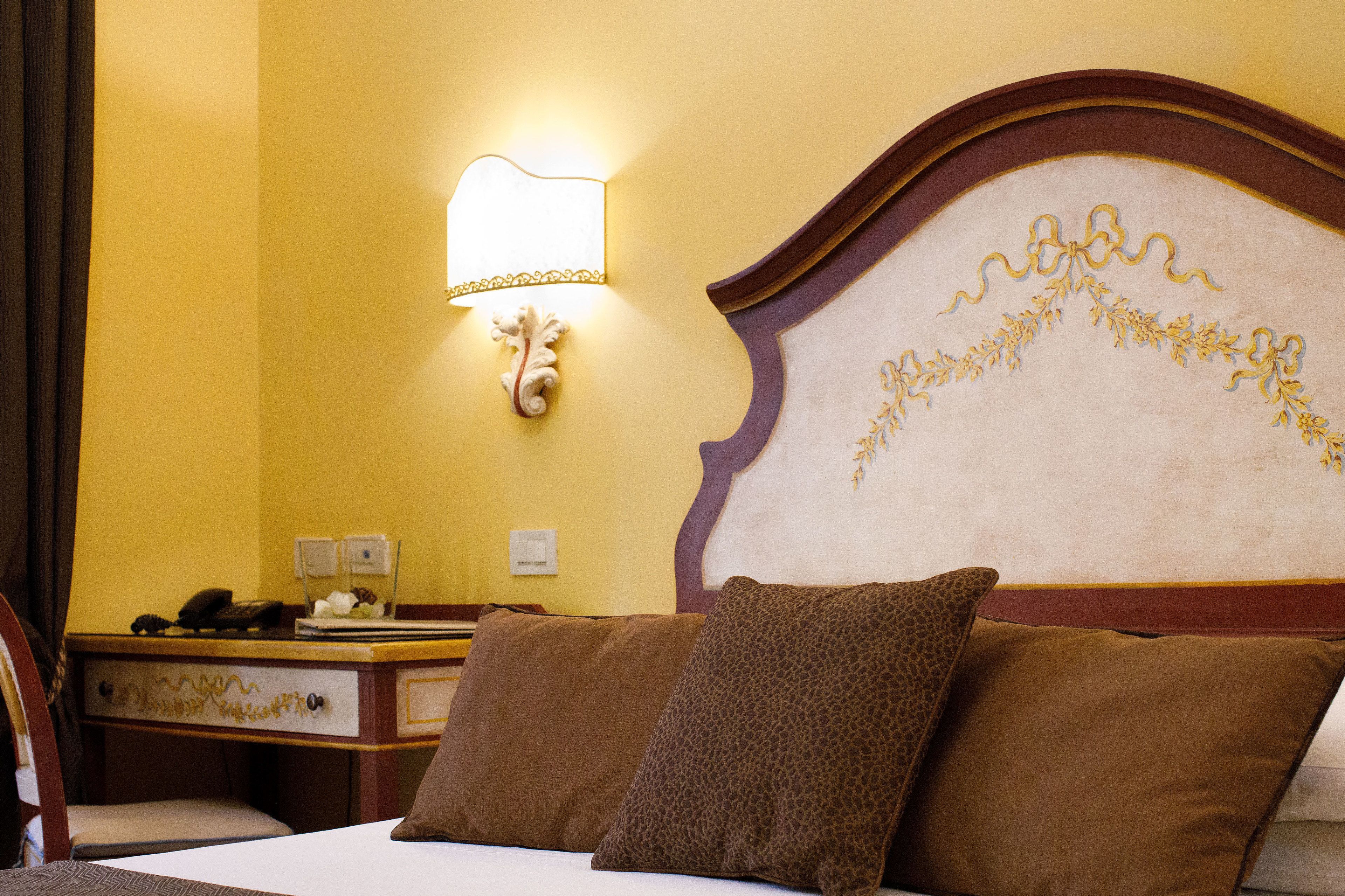 A hotel room with a bed, two pillows, a nightstand, a lamp, and a desk with a telephone.