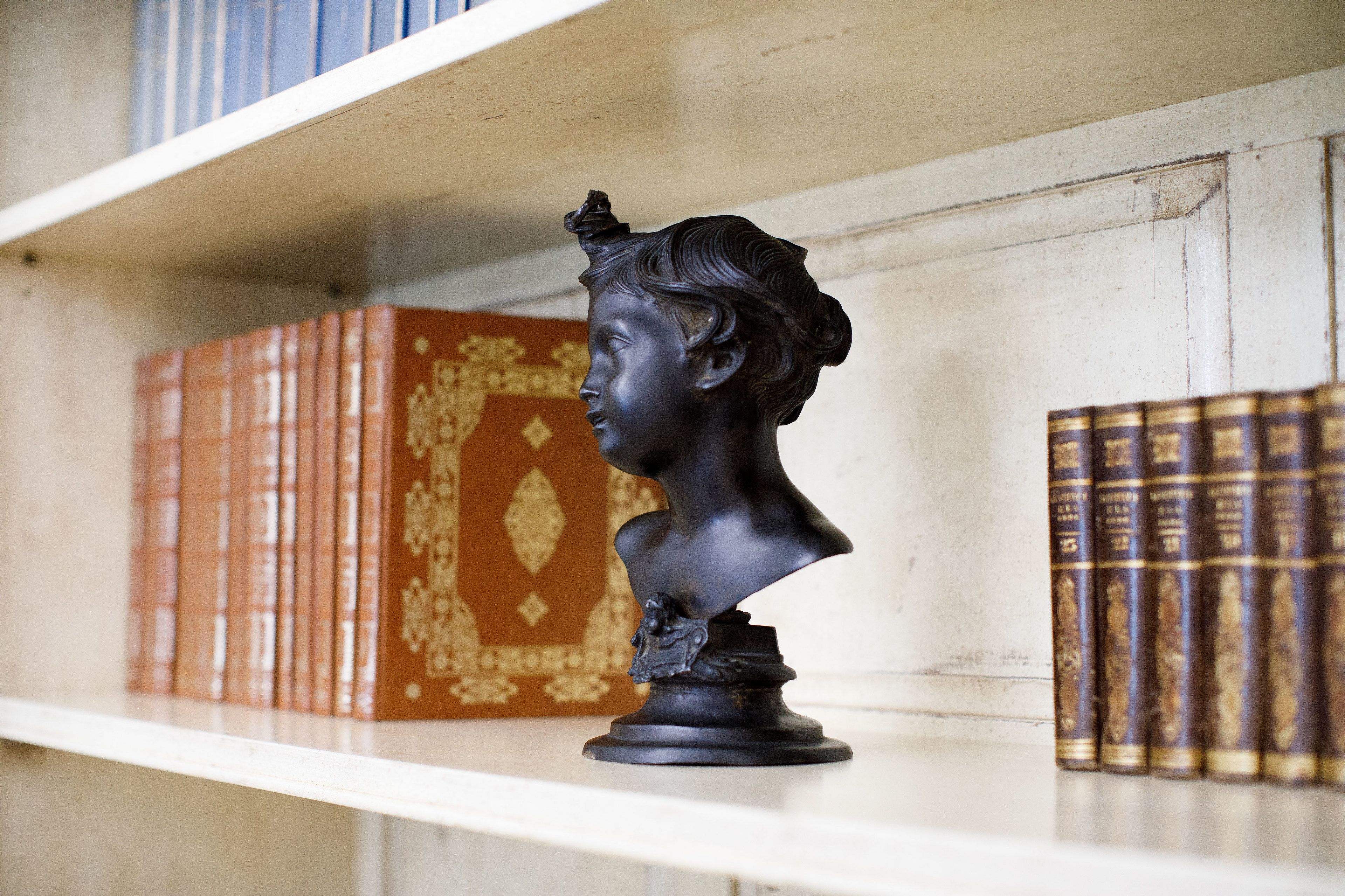A bust sculpture on a shelf with books behind it.