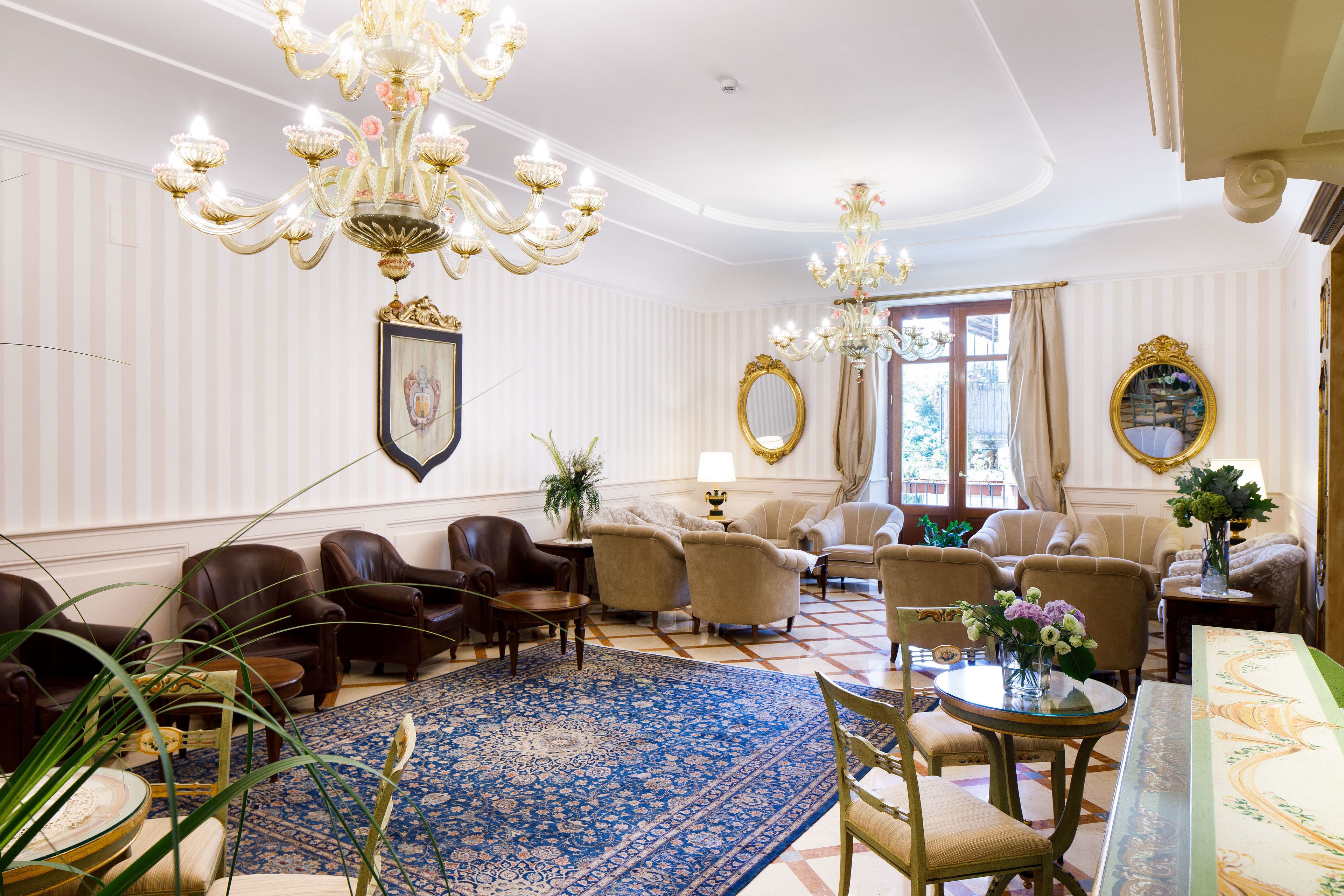 A spacious room with a large blue carpet, leather chairs, a chandelier, and a large mirror.