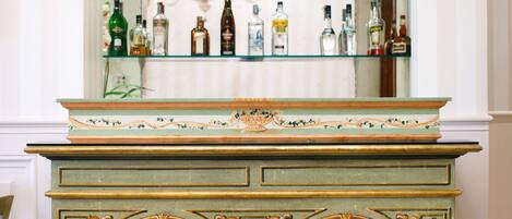 Una zona de bar con estantes llenos de botellas de licor, un mueble decorativo con motivos florales y una silla en primer plano.