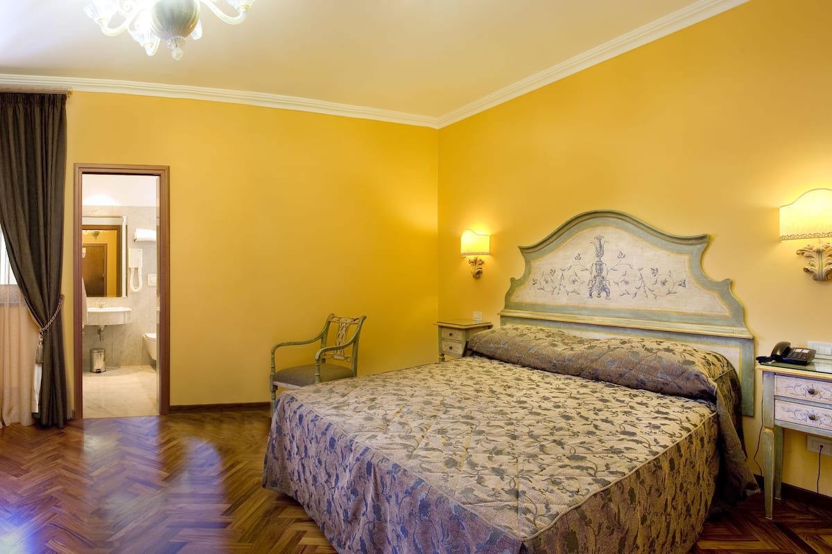 Un dormitorio con cama, escritorio, silla, mesita de noche y lámpara de pared.