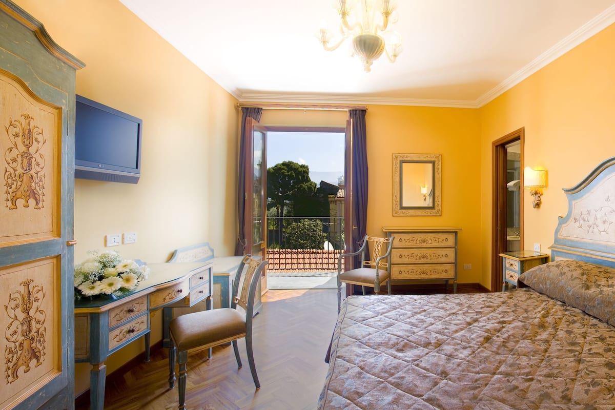 Habitación de hotel con cama, escritorio, silla, cómoda, espejo y candelabro.