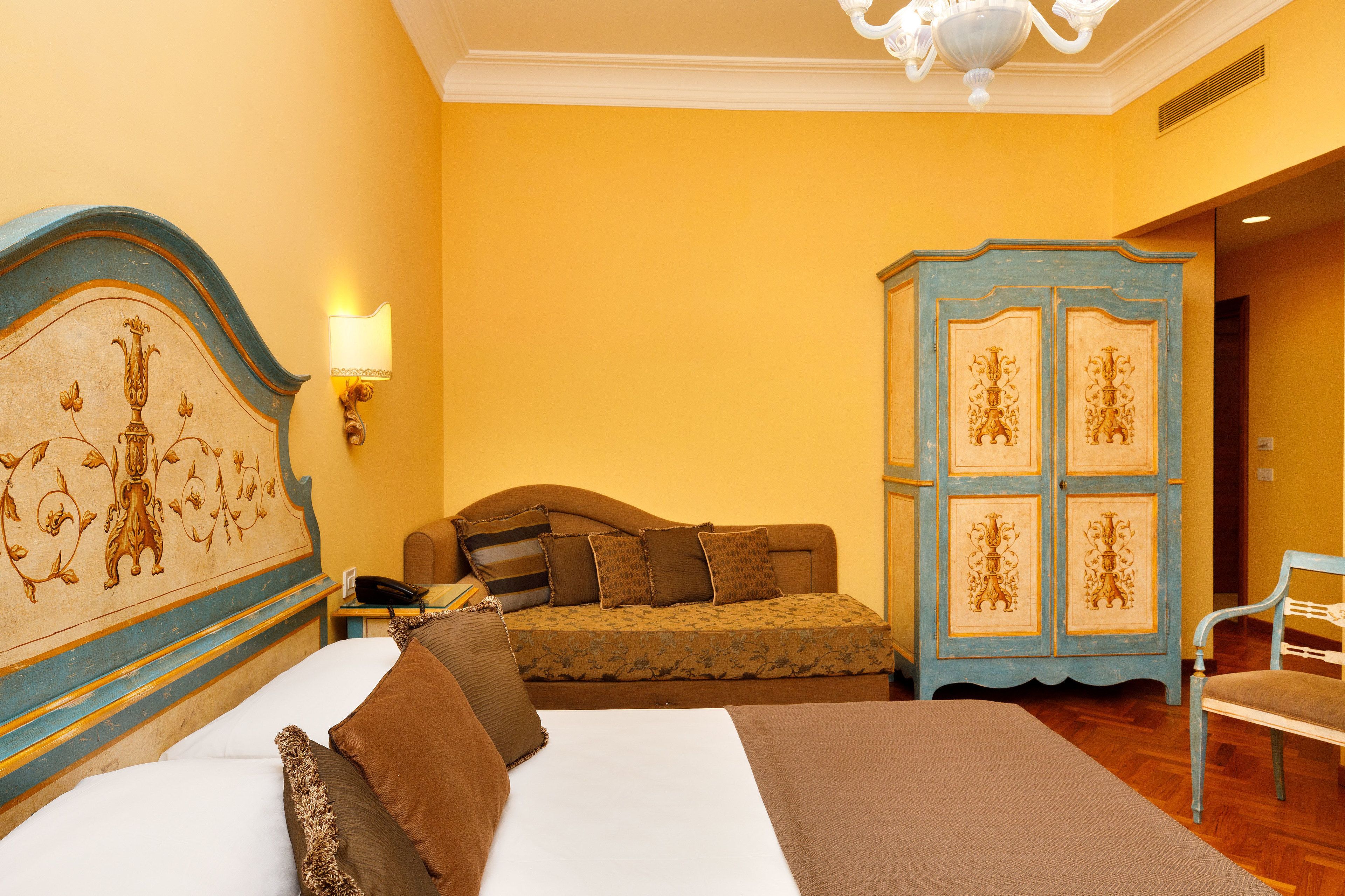 A hotel room with a large bed, a sofa, a wardrobe, and a chair.