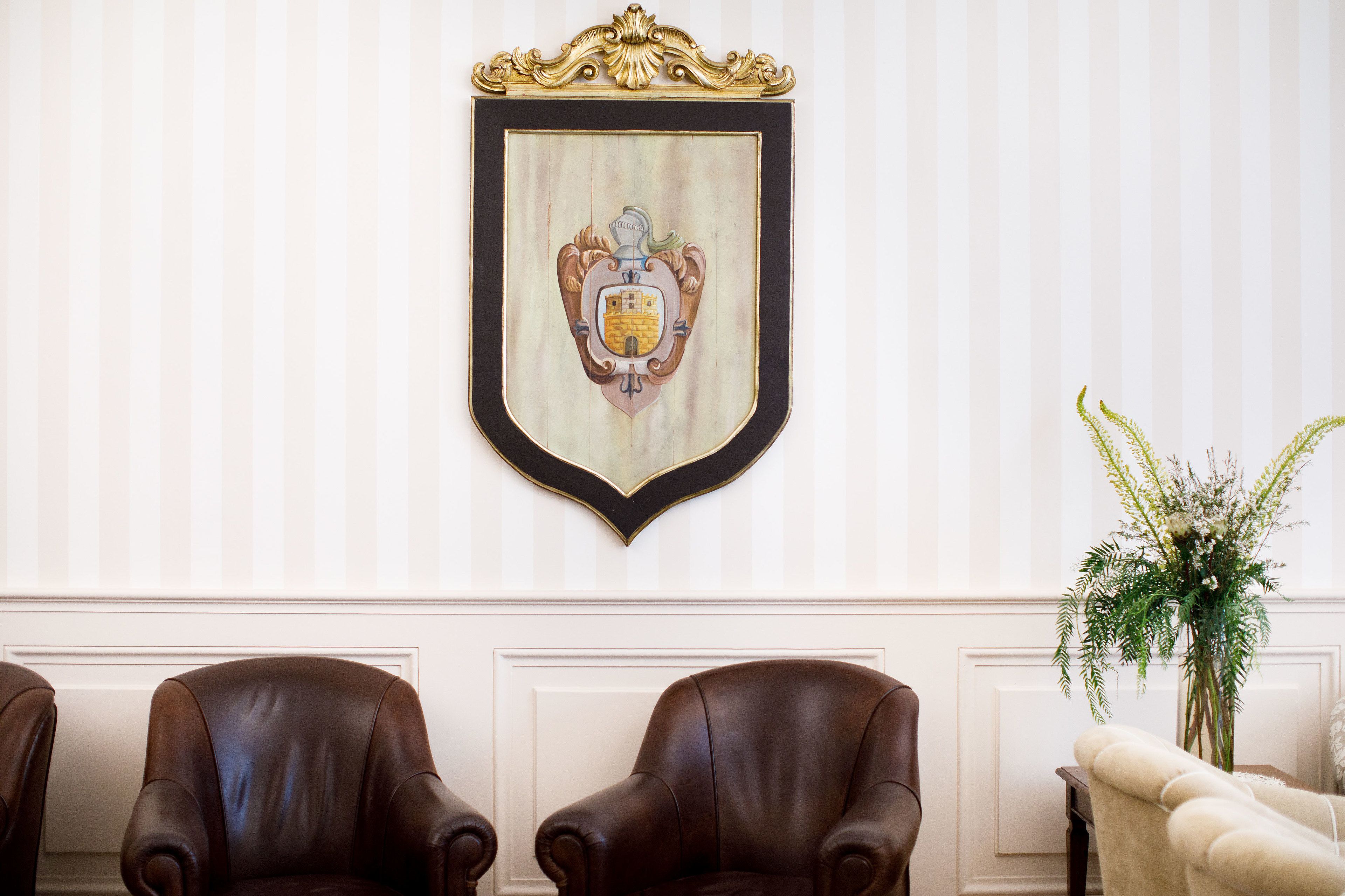 A room with a framed coat of arms on the wall, two leather armchairs, and a white armchair.