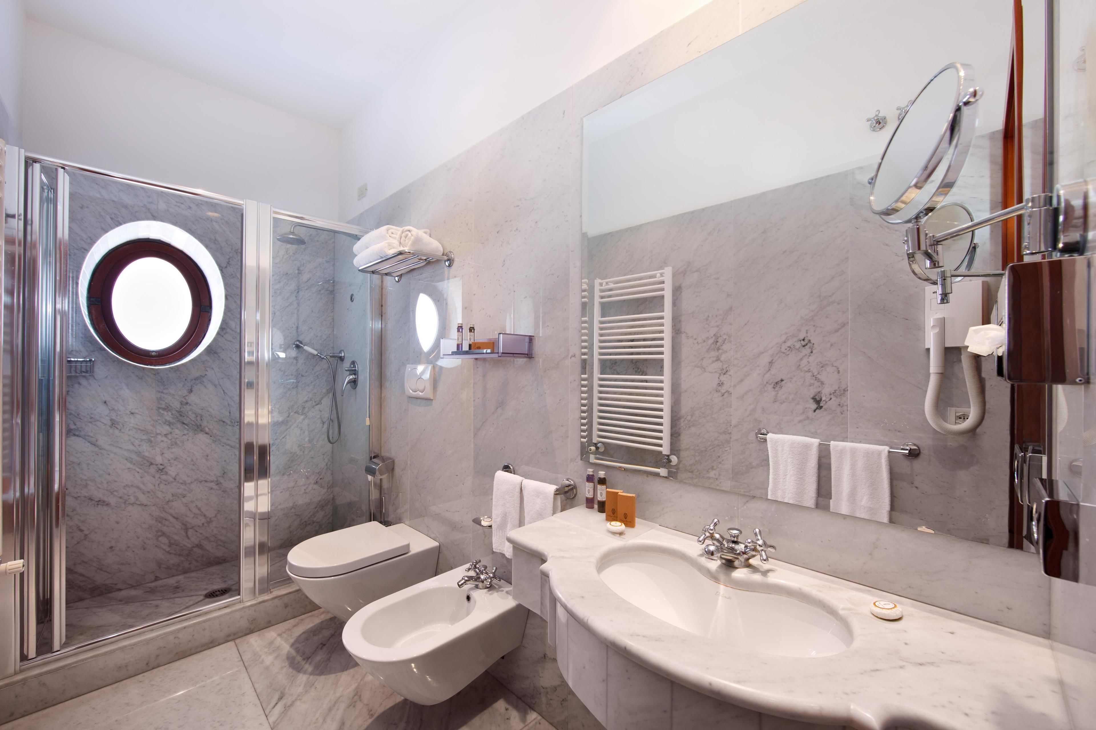 Un baño moderno con ducha de vidrio, un bidé, dos lavamanos y un espejo grande.
